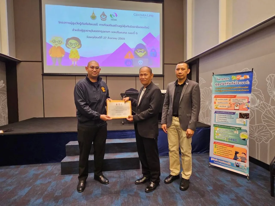 ภาพมอบเกียรติบัตรวิทยากรหน้าป้ายโครงการผู้สูงวัยรู้ทันภัยไซเบอร์